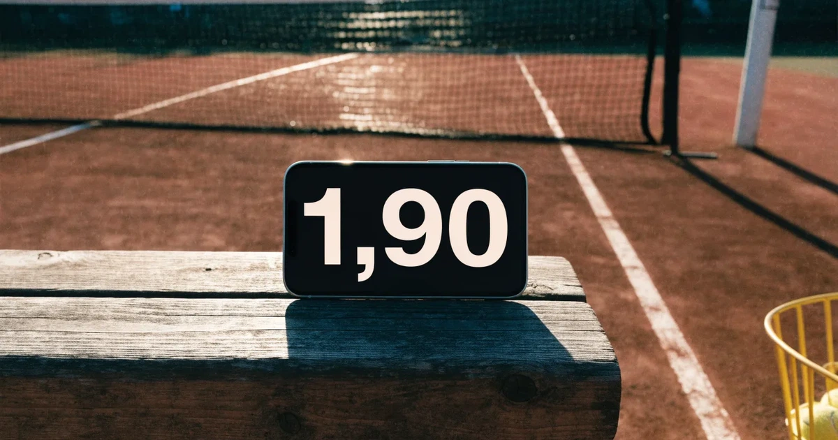 Ein Sandplatz mit frisch gezogenen Linien in der Nachmittagssonne, Netz und Ballkorb am Rand, keine Menschen.