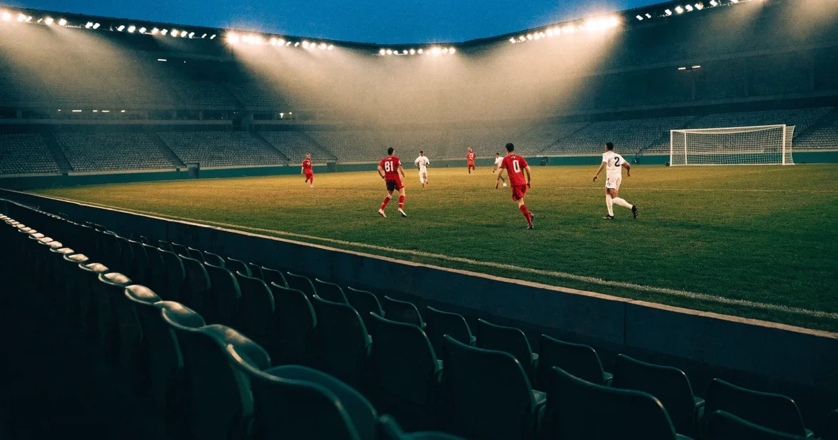 Leere Sitzreihen eines großen Stadions unter Flutlicht, dahinter die ferne Sicht auf den hell beleuchteten Rasen nach Sonnenuntergang.
