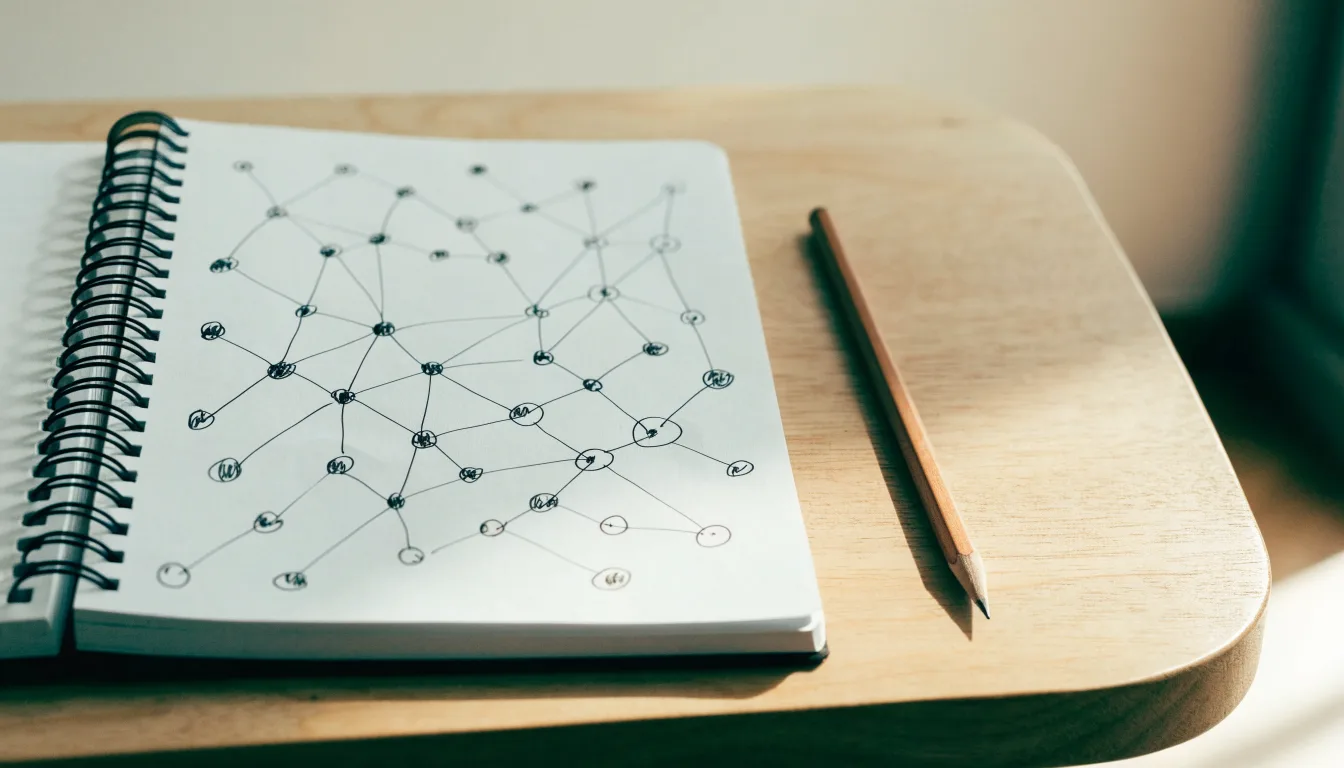 Ein Notizbuch mit handgezeichneten Knoten und Linien liegt neben einem Bleistift auf einem Schreibtisch.