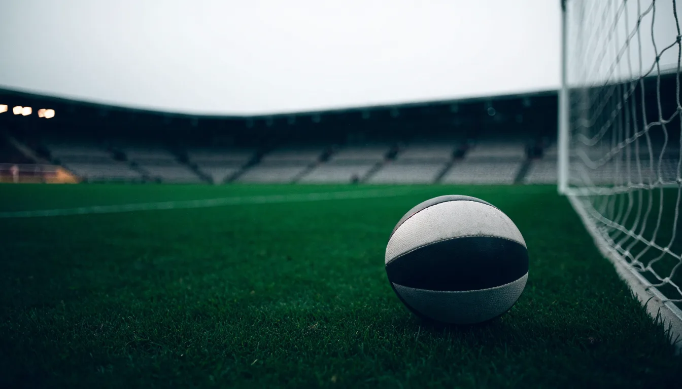 Ein Fußball auf einem Rasen, im Hintergrund ein leeres Stadion bei bewölktem Himmel.