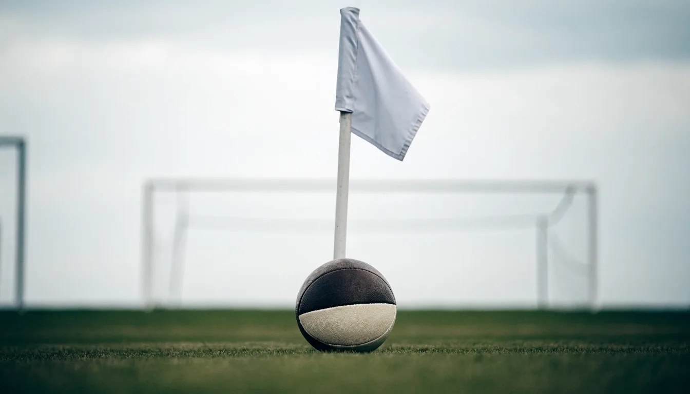 Ein Fußball liegt neben einer Eckfahne auf kurz gemähtem Rasen unter bewölktem Himmel.